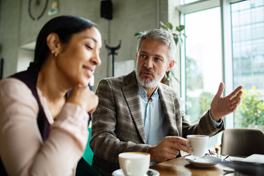 Mature man and adult woman discussing work in cafe, focused