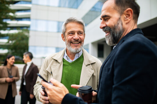 Mature men laughing with coffee outside modern office