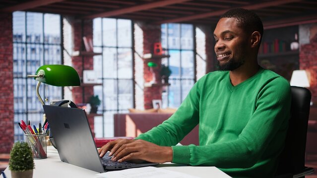 Black teleworker at home desk opening laptop to edit documents and solve daily tasks, updating reports and files. Young employee doing remote job and managing digital paperwork. Camera B. - Powered by Adobe