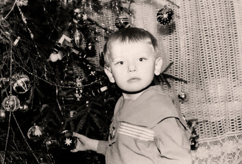 Vintage portrait of a little boy near a Christmas tree. Retro photo from 1970.