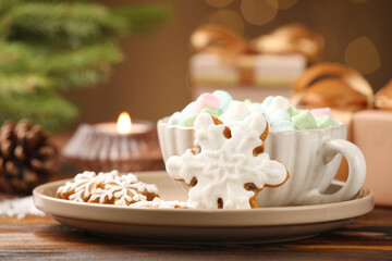 Tasty gingerbread cookies, marshmallows and Christmas decor on wooden table against blurred lights, closeup. Bokeh effect