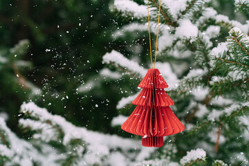 Red paper Christmas tree ornament on snowy pine branches. Festive composition, mockup for a New Year's card
