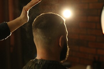 Hairstylist applying talcum powder onto man's hair at salon, closeup
