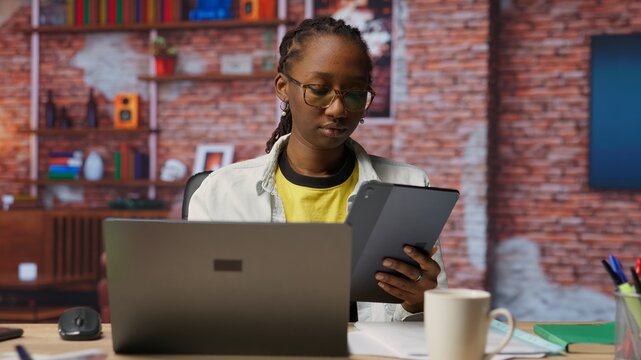 Woman at home taking break from work to look at social media feed on tablet. Remote employee at work in apartment office pausing tasks to use social network application on device, camera B