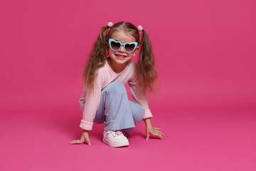 Smiling little girl in sunglasses on pink background