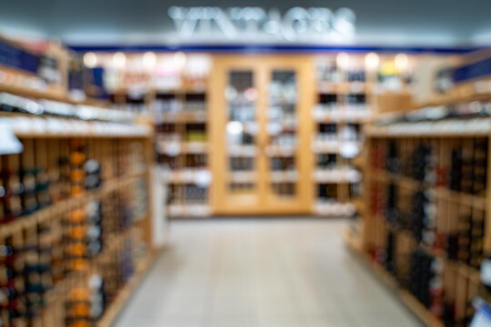 Blurred view of wine bottles on wooden store shelves.