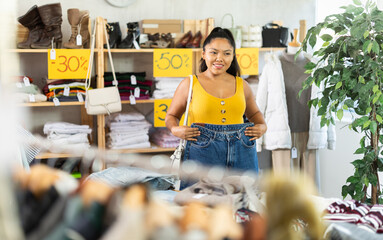 Young female shopper buying jeans in clothing store