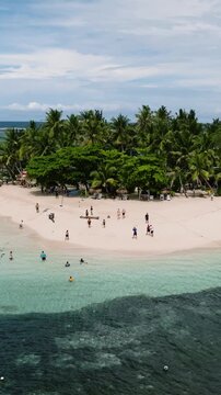 Beach on tropical island with palm trees, people swimming in turquoise sea and anchored boats nearby. Guyam Island. Siargao, Philippines.
