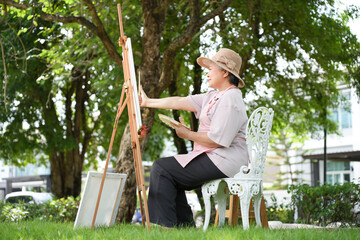 Senior woman painting on canvas in a garden setting, Elderly artist creating artwork outdoors in natural light, Mature woman enjoying outdoor painting activity in the park