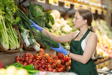 Supermarket employee carefully places green onion on shelves of a grocery supermarket