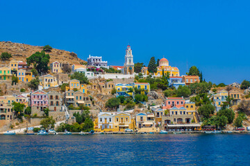 Landscape view of Symi town on Symi island with colorful neoclassical houses and a church tower, Greece