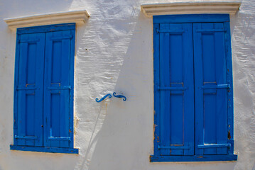 Windows with blue closed shutters on a white wall, Symi island, Greece