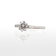 White gold solitaire ring with central diamond photographed on a white background with reflection