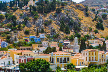 Landscape view of Symi town on Symi island with colorful neoclassical houses and a church tower, Greece