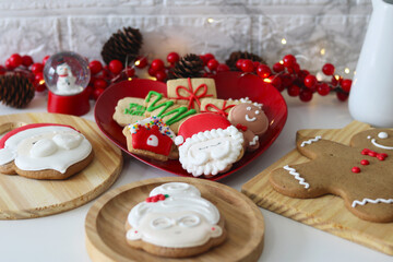 A festive Christmas display with several decorated cookies (Santa Claus, Mrs. Claus, gingerbread man) on wooden boards and a heart-shaped plate, surrounded by Christmas decorations.