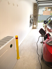 vertical shot Electric car EV plugged in on charge in a garage with active solar battery wall installation green light showing activity