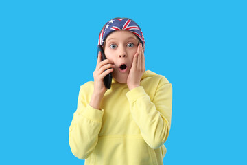 Surprised little girl talking by mobile phone on blue background