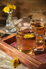 Board with glass cups of healthy dandelion tea on wooden table
