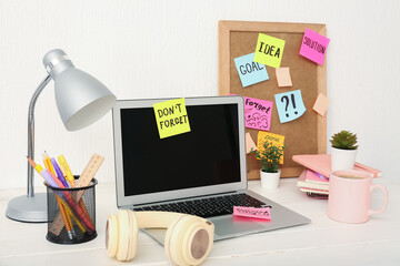 Laptop with sticky notes, headphones, coffee cup and stationery on white wooden table