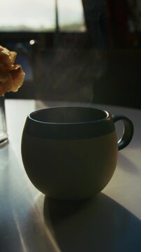 Quiet moment of a tea cup set on a kitchen table as steam rises gently, beautifully backlit by soft autumn morning sunlight, creating a serene, cozy atmosphere.