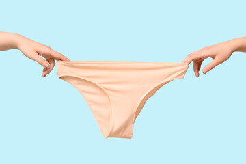 Female hands with cotton panties on color background, closeup