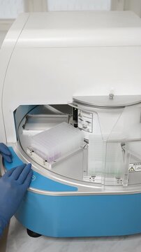 Scientist loading 96 well plate into automated PCR workstation inside modern laboratory.