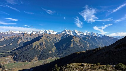 Obraz premium Snow-capped mountains and lush green valleys beneath a blue sky with clouds, mountain landscape, scenic view, and natural environment.