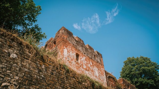 Ancient brick structure with arched openings against a blue sky and green trees. Historical ruins and architecture. - Powered by Adobe