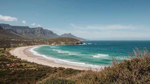 Coastal landscape with a sandy beach, waves, and mountains in the background. Nature scene with ocean and shoreline. Scenic view of the coastline and ocean horizon.