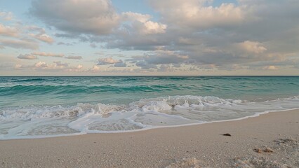 Fototapeta premium Beach shoreline with waves and clouds in the sky.