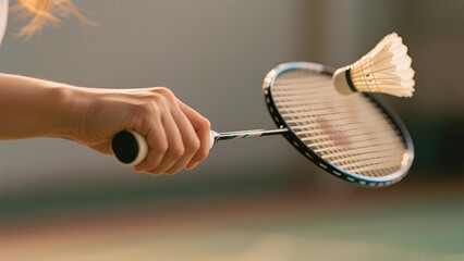 Close-up of a hand holding a badminton racket with a shuttlecock in mid-air during a game.