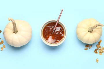 Bowl of sweet pumpkin jam and seeds on blue background