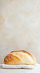A loaf of freshly baked bread rests on a white linen cloth, set against a neutral, textured background.