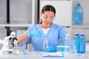 Happy female young scientist with professional glassware examining water quality in research laboratory