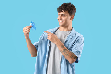Young man pointing at blue ribbon on color background. Prostate cancer awareness concept