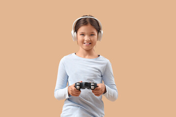 Little girl in headphones playing video game on beige background