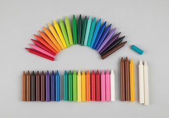 Obraz premium Assorted crayons arranged in rows and a semi-circle, displaying a variety of colors on a neutral background.