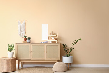 Interior of stylish room with wooden cabinet, pouf and houseplants near beige wall