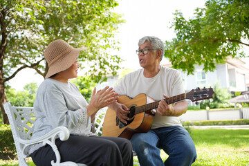 Senior Couple Enjoying Music Together In The Garden, Elderly Man Playing Guitar While Woman Applauds, Happy Seniors Spending Quality Time With Music Outdoors