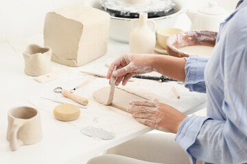 Young female potter with cut clay slab on table in home studio, closeup