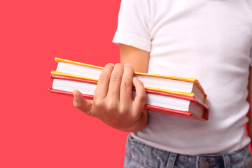 Cute little girl holding books on red background