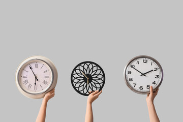 Female hands holding different wall clocks on grey background
