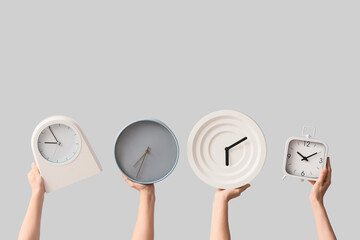Female hands holding different wall and alarm clocks on grey background