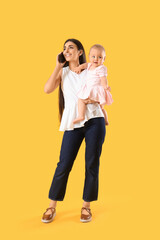 Young business mother with cute little baby talking by phone on yellow background