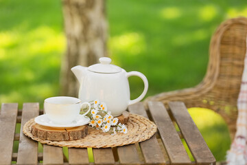 Chamomile flowers with cup and teapot on wooden coffee table in park, outdoors