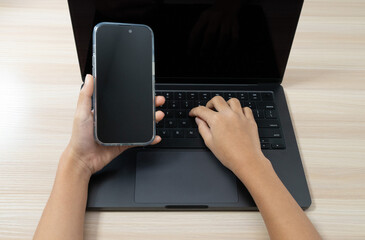 Hands using laptop and holding smartphone for multitasking