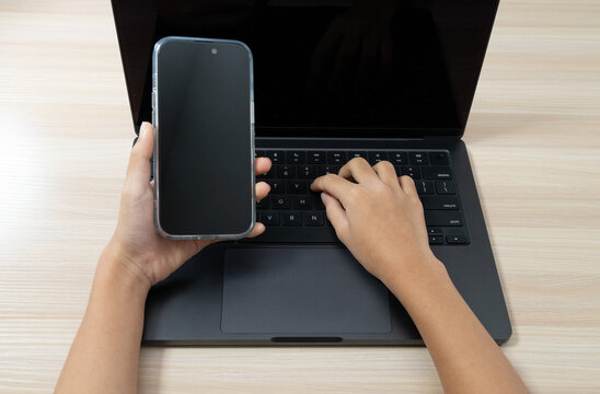 Hands using laptop and holding smartphone for multitasking
