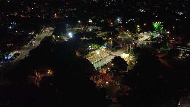 Night pan of Las Am&eacute;ricas showing the park, plaza, and Maya sculpture with Christmas lighting and urban movement. Shot with a 4K UHD drone.