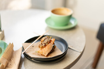 Open sandwich with smoked salmon, greens and seeds served on plate beside coffee cup in cafe setting with natural light and indoor atmosphere