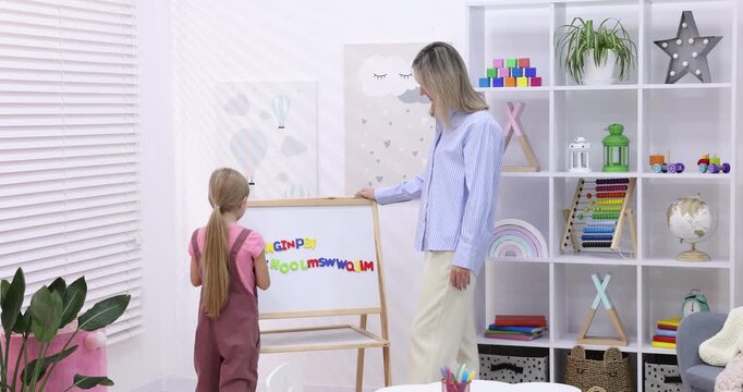 Speech therapist teaching girl alphabet near whiteboard with letters indoors